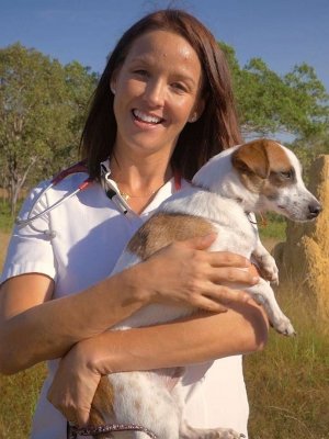 Dr Susanne Samuelsson stands in the Australian outback holding a dog.
