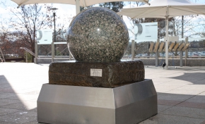 A large granite stone ball sitting on a large slab of stone, which intern sits within a stainless steel bin. Water flows from under the granite and over the stone to the bin.