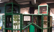 A children's play gym made of black plastic netting, green padded framework and a purple cargo net.