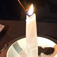 A vertical cylindrical paper tube sitting on a white plate, has a flame at the top.