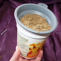 A plastic cup held in someones hand, has a funnel on the top and sand in the funnel.