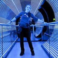 A teenage girl holds onto hand rails in a large cylinder lined with blue and white led lights. She is leaning to the right.