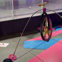 A wheel sits on a cable tightrope, with two masses extending from the wheel so they hang below the cable tightrope