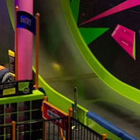 A bright green and steel slide, with an entrance gate and pink pole in the foreground