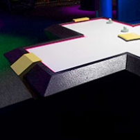 A cross shaped black and yellow air hockey table with a white surface.