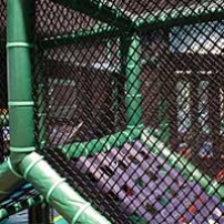 A children's play gym made of black plastic netting, green padded framework and a purple cargo net.