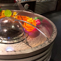 water flowing out of stainless steel tubes onto a perspex dome and into a doughnut shaped basin. There are coloured toys in the basin.