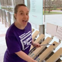 A woman wearing a t-shirt is playing a rock xylophone.