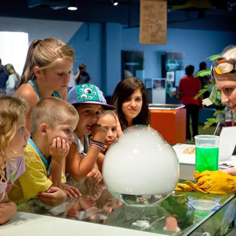Children watch a Questacon staff member make a bubble on top of a fish bowl full of dry ice