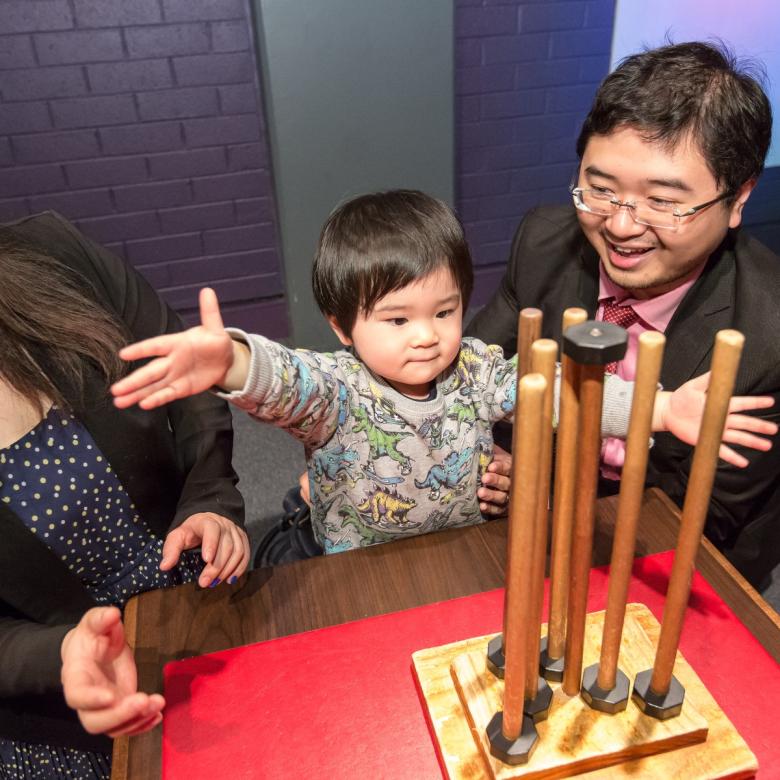 Two parents and a child play with balancing objects