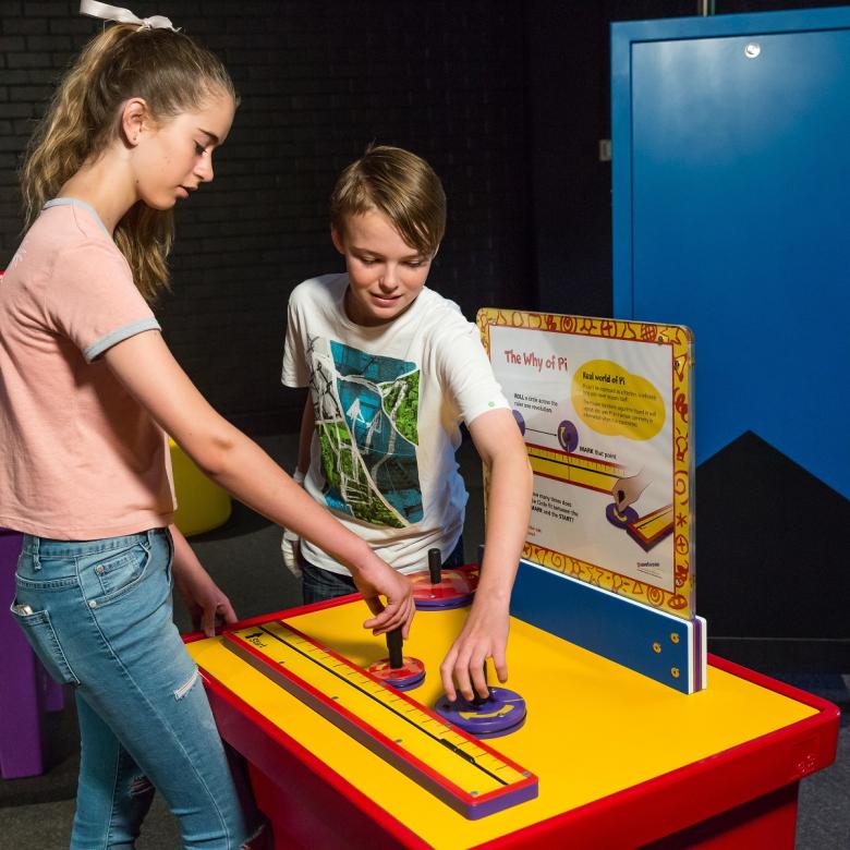 Two children look down on a yellow table and use measurement instruments