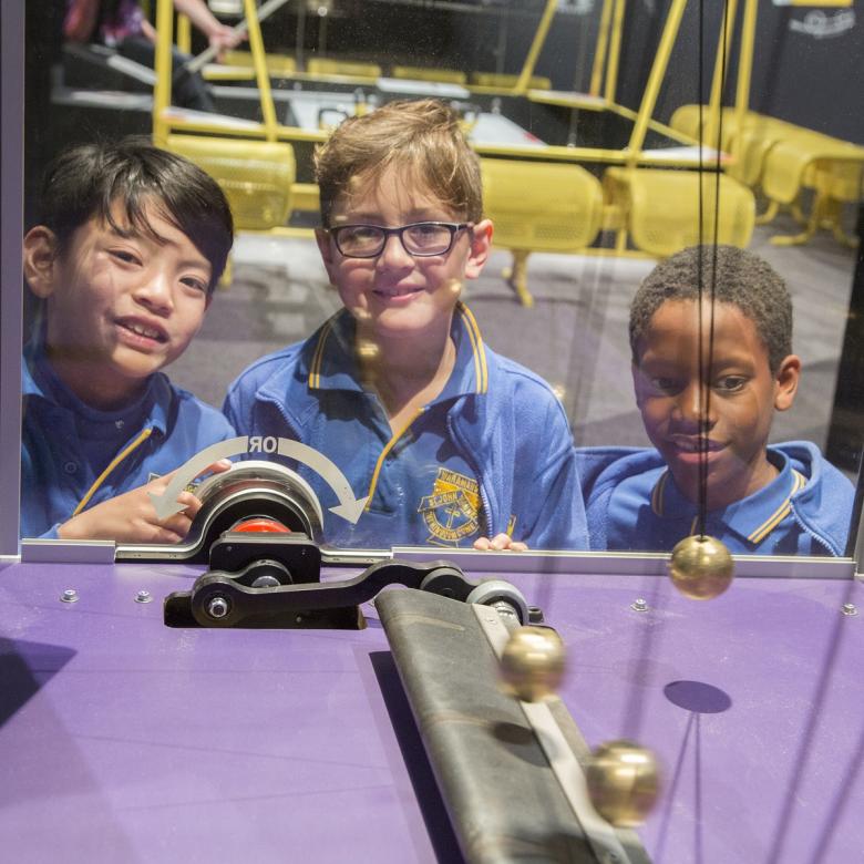 Three children watch pendulums swing in an exhibit