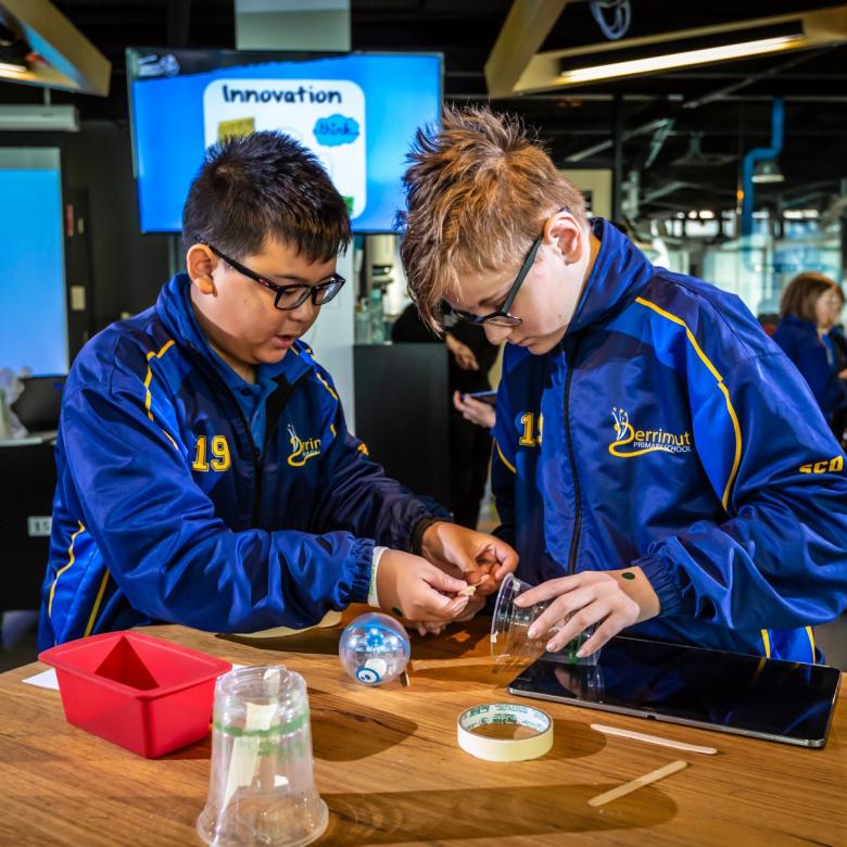 Two students in blue jackets work together to build a prototype for their Sphero (a round ball-like robot)