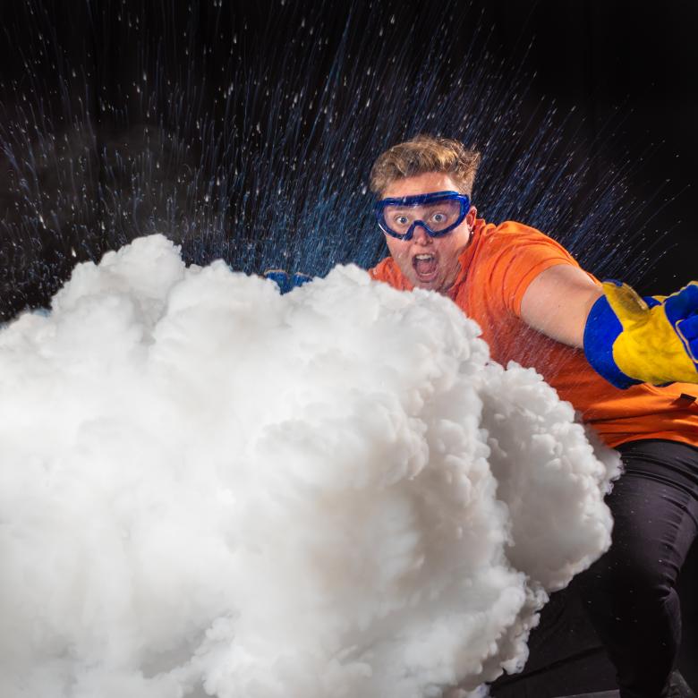 An excited Questacon Science Circus presenter standing behind a cloud of exploding liquid nitrogen