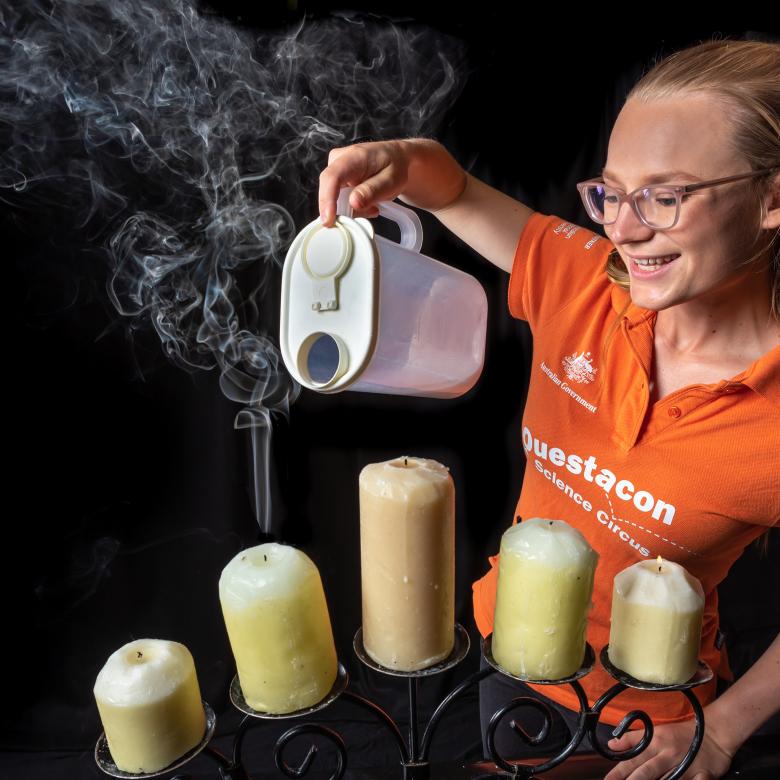 A Questacon Science Circus presenter extinguishing candles with a jug of Carbon Dioxide